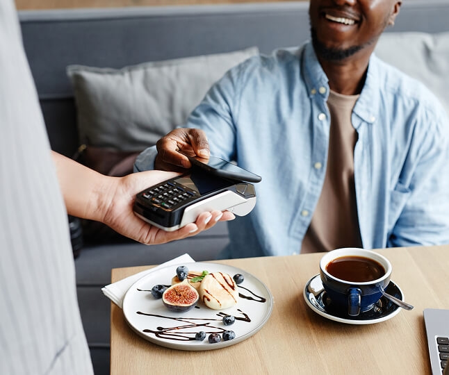 Homem sorrindo e pagando a conta com o celular
